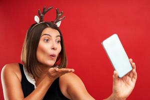 mulher adulta feliz em clima de natal tomando selfie sobre fundo vermelho foto