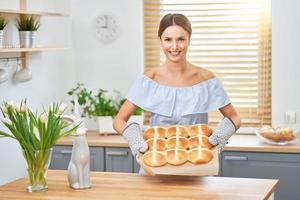 mulher adulta feliz preparando pães transversais quentes para a páscoa na cozinha foto