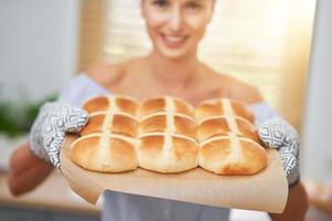 mulher adulta feliz preparando pães transversais quentes para a páscoa na cozinha foto