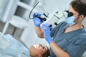 dentista verificando os dentes do paciente com microscópio no consultório de cirurgia foto