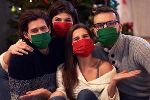 grupo de amigos usando máscaras comemorando o natal em casa foto