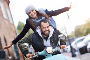 lindo casal jovem sorrindo enquanto andava de scooter na cidade no outono foto