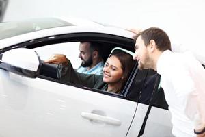 jovem vendedor confiante explicando as características do carro para os jovens proprietários atraentes foto