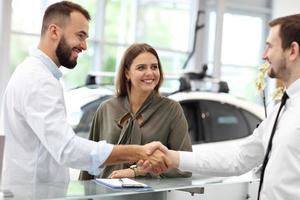 jovem vendedor confiante explicando as características do carro para os jovens proprietários atraentes foto