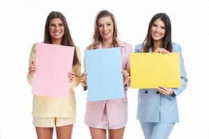 três mulheres em ternos pastel segurando outdoor posando sobre fundo branco foto