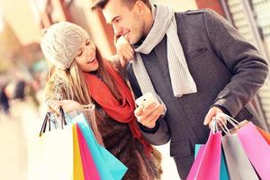 casal alegre fazendo compras na cidade com smartphone foto