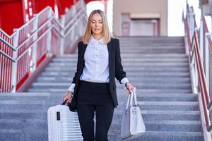 mulher elegante andando com bolsa e mala na estação ferroviária foto