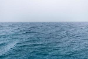 chuva sobre o mar tempestuoso, água azul do oceano e gotas de chuva. horizonte de vista para o mar sem fim, neblina e clima relaxante enevoado. litoral abstrato foto