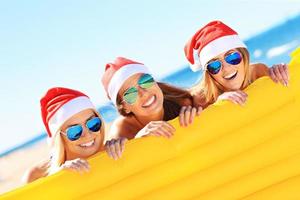 grupo de meninas com chapéu de Papai Noel se divertindo na praia foto