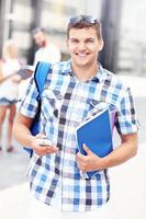 estudante feliz em pé no campus com seu smartphone foto