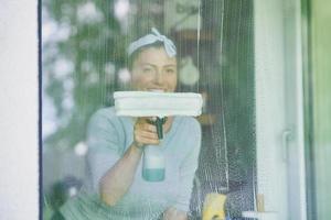 jovem mulher limpando janela na cozinha foto