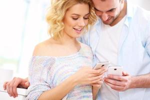 casal feliz usando telefone inteligente em casa