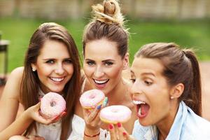 feliz grupo de amigos comendo rosquinhas ao ar livre foto