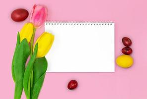 caderno em branco com espiral para texto, tulipas com ovos coloridos em um fundo rosa. cartão de páscoa. copie o espaço foto