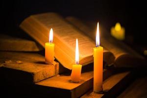 luz de vela com a bíblia sagrada e cruz ou crucifixo sobre fundo de madeira velho na igreja. luz de velas e livro aberto no estudo de cristianismo de mesa de madeira vintage e leitura em casa. conceito de religião de cristo foto