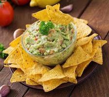 abacate guacamole, limão, tomate, cebola e coentro, servido com nachos - lanche mexicano tradicional foto