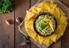 abacate guacamole, limão, tomate, cebola e coentro, servido com nachos - lanche mexicano tradicional foto