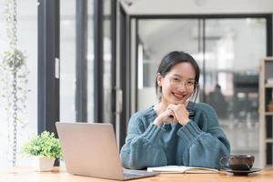 estudante de belas mulheres estudando on-line faz anotações em seu laptop para coletar informações sobre seu rosto sorridente de trabalho e uma postura de estudo feliz. foto
