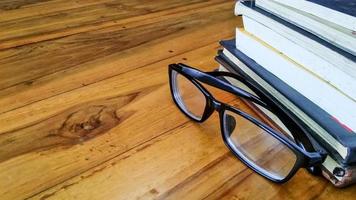 óculos e livros sobre uma mesa de madeira com espaço de cópia foto