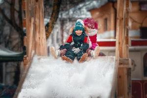 menina e menino sentado em uma colina de neve foto