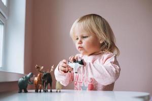 menina criança em rosa brincando com brinquedos de animais na mesa no quarto das crianças em casa foto