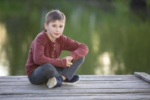 um belo menino feliz está sentado em uma ponte de madeira. foto
