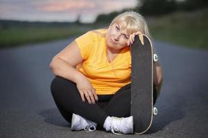 mulher europeia de meia-idade com excesso de peso, em um agasalho com um skate, pratica esportes. foto