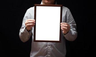 um diploma em branco ou um certificado de maquete na mão de um empregado homem vestindo camisa em fundo preto. a moldura vertical está vazia e o espaço da cópia. foto