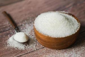 açúcar na colher e tigela de madeira, açúcar branco para alimentos e doces sobremesa monte de açúcar cristalino granulado foto