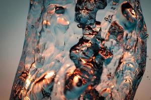 jatos de água com muitas gotas e bolhas sob os raios do sol sobre um fundo azul. um grande plano a textura das ondas de água de uma grande fonte foto