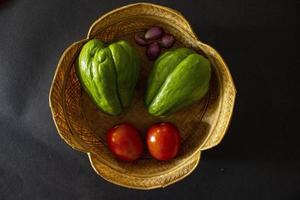 tomates tropicais com jipang ou labu siam ou chuchu e cebola são servidos em uma cesta isolada em fundo preto foto