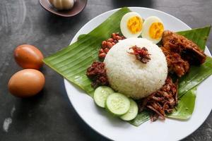 nasi lemak, é ovos cozidos malaios tradicionais, feijão, anchovas, molho de pimenta, pepino. do prato servido na folha de bananeira foto