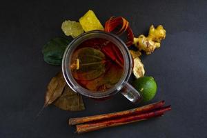 wedang uwuh é uma bebida tradicional à base de ervas da Indonésia. feito de folhas de canela, noz-moscada e cravo. outro ingrediente é a madeira da árvore secang, gengibre e torrões de açúcar em fundo preto foto