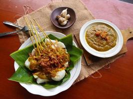 sate padang ou satay padang é satay de carne picante de padang, oeste de sumatra. servido com molho picante de curry e bolo de arroz, lontong em folha de bananeira. isolado no fundo branco foto