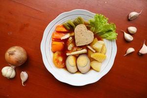 selat solo é uma salada tradicional da indonésia. feito de ovos cozidos, grão de bico cozido, cenoura cozida, batatas fritas e alface, bife ou bistik. servido na mesa de madeira foto