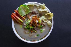 sop kaki kambing uma comida tradicional de betawi, jacarta indonésia, feita de carneiro ou cordeiro, miudezas, especiarias. isolado em fundo preto. esta comida é como ensopado de cordeiro em fundo preto foto