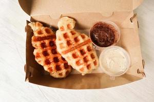 croissant waffle ou croffle com calda de chocolate servido em caixa e fundo branco foto