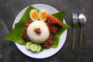 nasi lemak, é ovos cozidos malaios tradicionais, feijão, anchovas, molho de pimenta, pepino. do prato servido na folha de bananeira foto