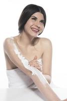 linda mulher de pele aplicando loção corporal em fundo branco foto