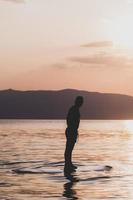 bonito homem desportivo está andando de caiaque no pôr do sol foto