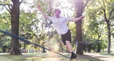 jovem equilibrando e pulando no slackline. homem andando, pulando e equilibrando-se na corda no parque. foto