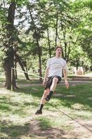 jovem equilibrando e pulando no slackline. homem andando, pulando e equilibrando-se na corda no parque. foto