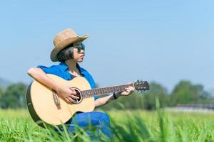 mulheres de cabelo curto usam chapéu e óculos de sol sentam-se tocando violão no campo de grama foto