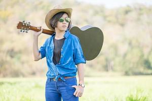 mulher usa chapéu e carrega seu violão no campo de grama foto