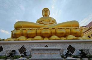 vista frontal estátua dourada do grande buda phra buddha dhammakaya thep mongkol, traduzir linguagem no templo wat pak nam phasi charoen. céu de luz solar e fundo de nuvens foto