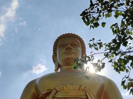 rosto de estátua de buda grande dourado phra buddha dhammakaya thep mongkol no templo wat pak nam phasi charoen. céu de luz solar e fundo de nuvens foto