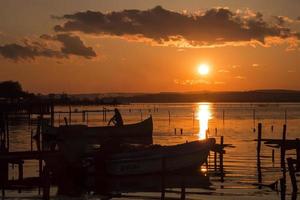 belo pôr do sol do lago de longa exposição com barco e pescador. foto