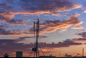 silhueta de transmissores gsm no prédio de escritórios do telhado em nuvens incríveis foto