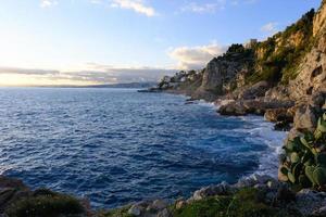 litoral rochoso do mar ao pôr do sol, vista do mar, vista da costa. paisagem com água, montanhas e céu azul ao ar livre. foto