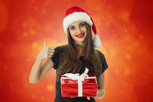 menina sorrindo com chapéu de Papai Noel com presente vermelho foto